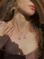 Woman wearing a gold necklace with a floral pendant, close-up of neck and chest.